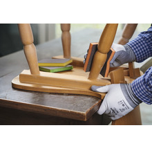 Eine Person schleift einen Holzstuhl mit einem Schleifklotz. Schleifpads liegen bereit.