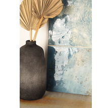Dekorative blaue Fliesen neben einer grauen Vase mit getrockneten Palmblättern.