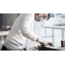 Frau schleift Holzwerkstück mit Schleifpapier, Schutzmaske und Handschuhe