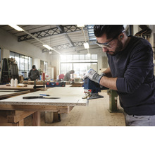 Ein Mann sägt in einer Werkstatt mit einer Stichsäge ein Werkstück.