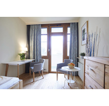 Helles Zimmer mit Schreibtisch, Stühlen, Kommode und Balkontür