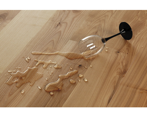 Ein umgefallenes Glas auf einem Holzboden, das Wasser verschüttet.