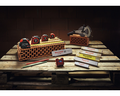 Maurerwerkzeugsortiment auf Holzpalette mit Bandmaßen, Messrad, Gliedermaßstäben, Bleistiften und Digitaluhr