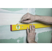 Eine Wasserwaage wird an einer Wand mit Gipsplatten angelegt, um eine Linie mit einem Bleistift zu zeichnen.