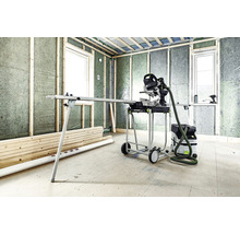 Raum im Rohbau mit Paneelen, Fenstern, Holzstapel, Paneelsäge auf Arbeitstisch mit Rädern und Staubsauger