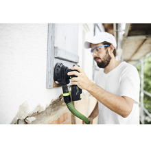 Ein Mann benutzt einen Schleifer an einer Hauswand mit Fensterladen