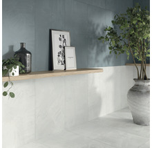 Badezimmer mit weißen Wand- und Bodenfliesen, dekoriert mit Pflanzen und Bilderrahmen auf einem Regal.