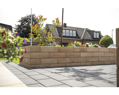 Gartenmauer aus Steinblöcken mit Pflanzen und gepflastertem Boden