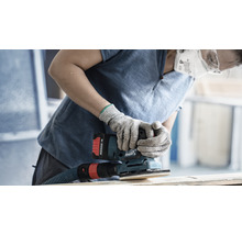 Eine Person trägt eine Schutzmaske und Schutzbrille und verwendet einen Schwingschleifer zum Schleifen eines Holzstücks.