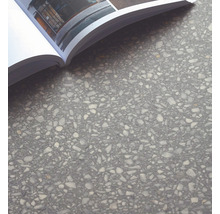 Nahaufnahme einer grauen Bodenfliese mit Steinchenstruktur und offenem Buch.