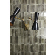 Wand mit rechteckigen Fliesen und einer goldenen Wandlampe mit zwei Leuchtenarmen.