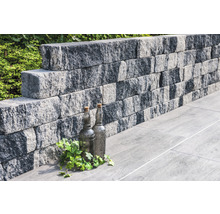 Stützmauer aus Betonsteinen mit dekorativen Flaschen und Pflanzen auf Bodenplatten