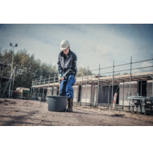 Bauarbeiter mischt Material in einem Eimer mit einem Rührgerät auf einer Baustelle.