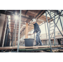 Frau mit Schaufel und Mörtelkübel auf einem Baugerüst