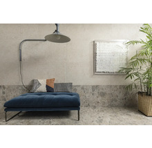 Wohnraum mit Couch, Kissen, Lampe, Pflanze und Wanddekoration vor Wand- und Bodenfliesen