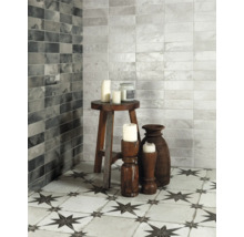 Badezimmer mit grauen und weißen Wandfliesen und Bodenfliesen mit Sternmuster, dekoriert mit Kerzen und Holzhockern.