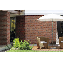 Terrasse mit Ziegelwand, Sonnenschirm und Korbsesseln.