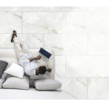 Mann liegt auf einem Sofa mit Laptop vor einem Hintergrund aus Wandfliesen