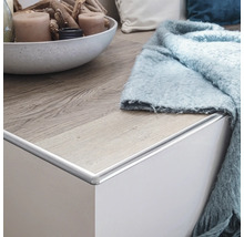 Abschlussleiste aus Aluminium an einer weißen Kommode mit Holzboden