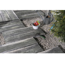 Gartenszene mit Gehwegplatten in Holzoptik, Kies, Gießkanne und Gartengeräten