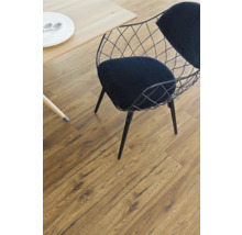 Detailaufnahme eines Zimmers mit Laminatboden, einem Tisch mit Geschirr und einem Stuhl mit Drahtgeflecht