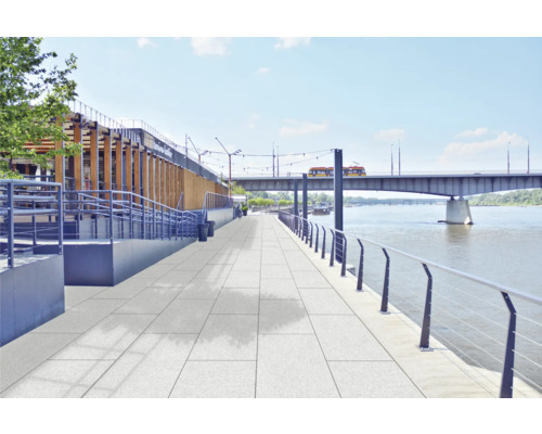 Terrasse mit Steinplatten am Flussufer und Brücke im Hintergrund.