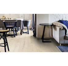 Innenaufnahme eines Wohnraums mit Esstisch, Stühlen, Beistelltisch und Sofa, die auf einem hellen Laminatboden stehen.