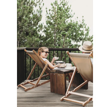 Szene auf einer Terrasse mit zwei Personen in Liegestühlen, einem Holztisch und Bäumen im Hintergrund