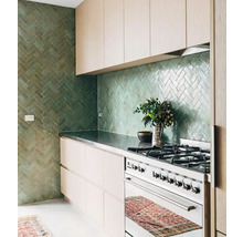 Helle Küche mit grünen Ziegeln im Fischgrätmuster, Kochfeld und Küchenschränken.