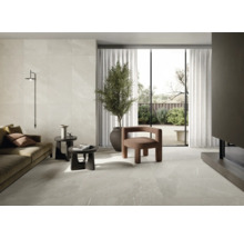 Helles Wohnzimmer mit Fliesenboden, Sofa, Sessel, Zimmerpflanze und Tageslicht.