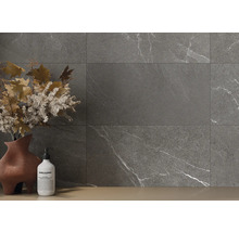 Graue Fliesen mit Marmoroptik an einer Wand, ergänzt durch eine Vase mit Blumenschmuck und eine Seifenflasche