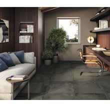 Wohnzimmer mit Couch, Tisch, Pflanzen, Schreibtisch, Stuhl und Fliesenboden.