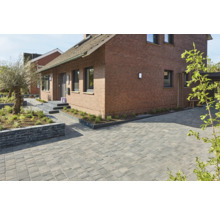 Gepflasterte Auffahrt vor einem Backsteinhaus mit Gartenbeeten.