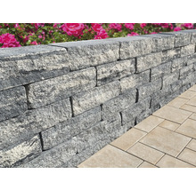 Nahaufnahme einer grauen Gartenmauer aus Steinen neben Pflastersteinen