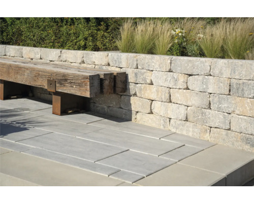 Außenbereich mit Mauer aus Steinblöcken, Bank aus Holz und Steinbodenplatten