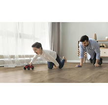 Vater und Sohn spielen mit Spielzeugautos auf einem Laminatboden im Wohnzimmer.