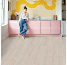 Helle Küche mit rosa Küchenzeile, Holzboden und einer Frau, die sich an die Küchentheke lehnt.