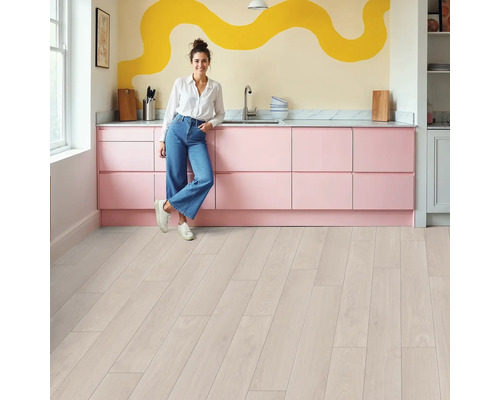 Helle Küche mit rosa Küchenzeile, Holzboden und einer Frau, die sich an die Küchentheke lehnt.