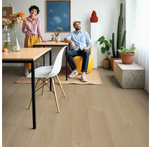 Wohnraum mit hellem Holzboden, zwei Personen, Tisch, Stuhl und Zimmerpflanzen.