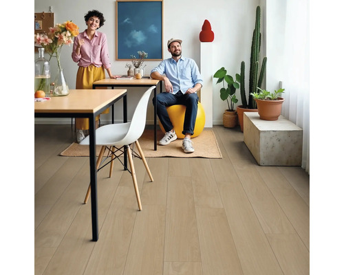 Wohnraum mit hellem Holzboden, zwei Personen, Tisch, Stuhl und Zimmerpflanzen.