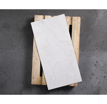 Eine einzelne helle Fliese mit Marmoroptik liegt auf einer Holzpalette.