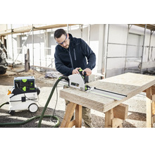 Ein Mann sägt Holz mit einer Handkreissäge und einer Führungsschiene von Festool, während ein Staubsauger daneben steht.
