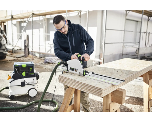 Ein Mann sägt Holz mit einer Handkreissäge und einer Führungsschiene von Festool, während ein Staubsauger daneben steht.