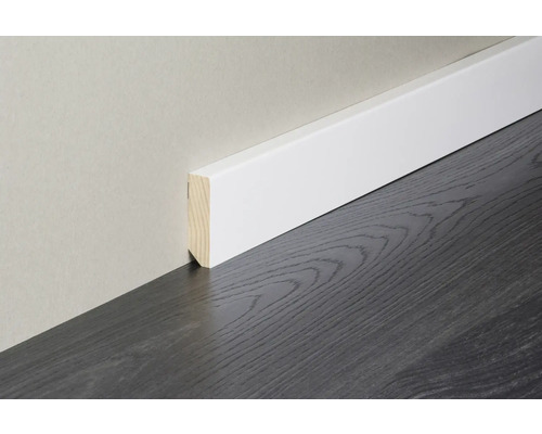 Weiße Sockelleiste mit Holzkern an einer hellen Wand auf dunklem Bodenbelag mit Holzoptik.