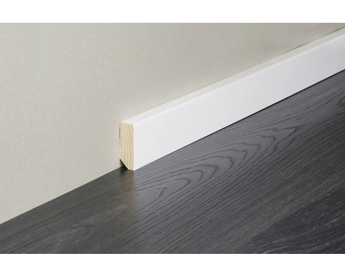 Weiße Sockelleiste aus Holz montiert an einer Wand über einem dunklen Bodenbelag.