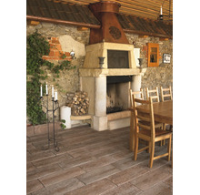 Terrasse mit Bodenplatten in Holzoptik, rustikalem Steinkamin mit Kupferhaube, Holztisch, Stühlen und einer Steinwand mit Efeu.