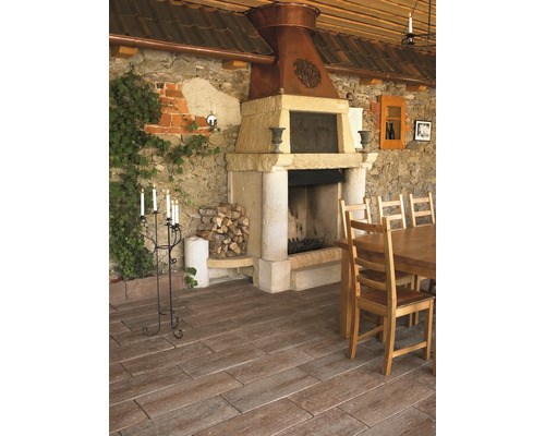 Terrasse mit Bodenplatten in Holzoptik, rustikalem Steinkamin mit Kupferhaube, Holztisch, Stühlen und einer Steinwand mit Efeu.