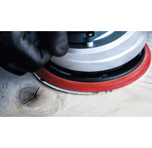 Draufsicht einer Hand mit Handschuh, die einen Exzenterschleifer auf einem Holzbrett bedient