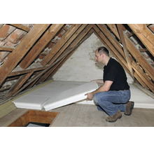 Mann verlegt Dämmplatten auf einem Dachboden mit Holzbalken.