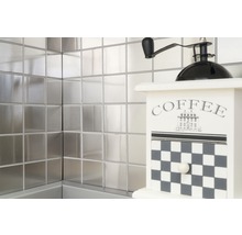 Quadratische Metallfliesen an der Wand mit einer dekorativen Kaffeemühle